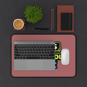 May include: A workspace setup featuring a laptop, mouse, and mousepad with the text "5 OU". A cup of coffee, a small plant, a notebook, and stationery are also present. The color scheme is primarily black, brown, and red.