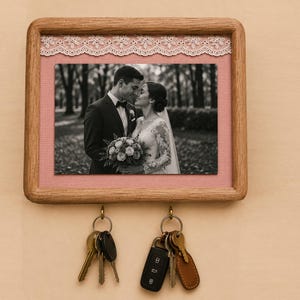 Peut inclure: Porte-clés en bois avec une photo de mariage encadrée, un fond rose et une bordure en dentelle blanche. Le porte-clés comporte deux porte-clés avec des jeux de clés et un porte-clés noir.