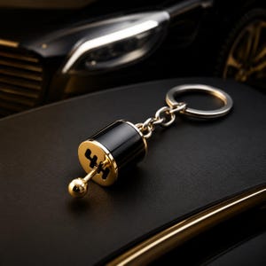 Peut inclure: Un porte-clés noir et doré en forme de levier de vitesse de voiture. Le porte-clés présente un motif de changement de vitesse doré et une petite boule dorée ronde au bout du levier. Il est attaché à un porte-clés argenté.