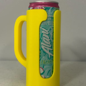 May include: A yellow can cooler with a handle, holding a can of Alani Energy drink. The can is teal and white with the word "Alani" in a stylized font. The top of the can is pink.