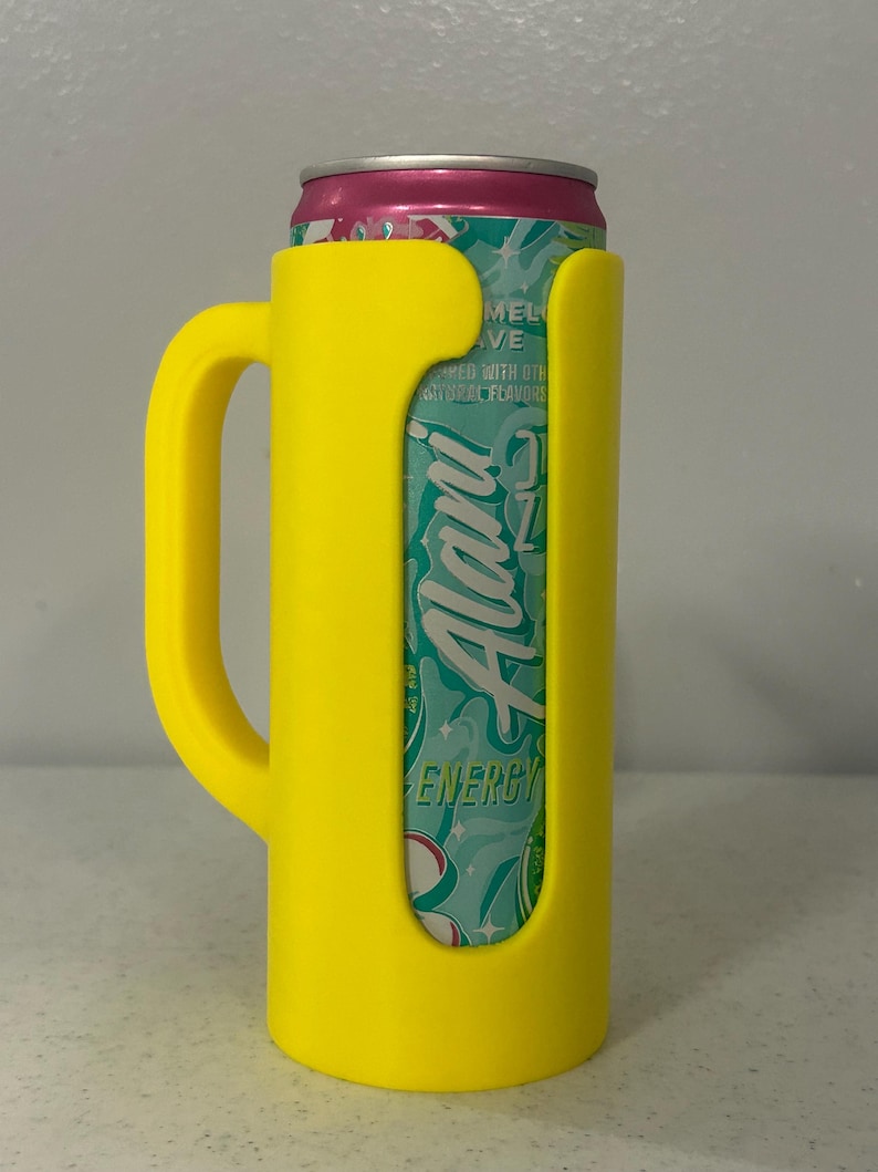 May include: A yellow can cooler with a handle, holding a can of Alani Energy drink. The can is teal and white with the word "Alani" in a stylized font. The top of the can is pink.