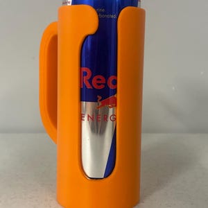 May include: An orange can cooler with a handle holds a Red Bull energy drink can. The can is blue and silver with the Red Bull logo and text. The cooler is made of plastic.