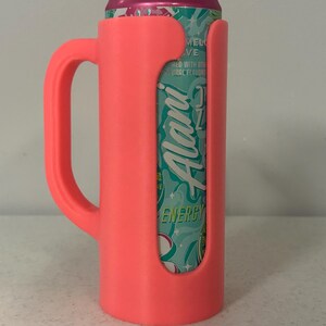 May include: A bright pink can cooler with a handle, holding a can of Alani Energy drink. The can is teal and white with the word "Alani" in a script font. The cooler has a cutout to show the can's design.