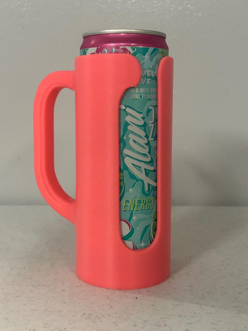 May include: A bright pink can cooler with a handle, holding a can of Alani Energy drink. The can is teal and white with the word "Alani" in a script font. The cooler has a cutout to show the can's design.