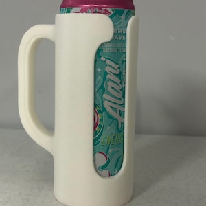 May include: A white 3D-printed can holder with a handle, designed to fit a standard beverage can. The can is visible through the holder's cutout, featuring a teal and pink label with the word "Alani".