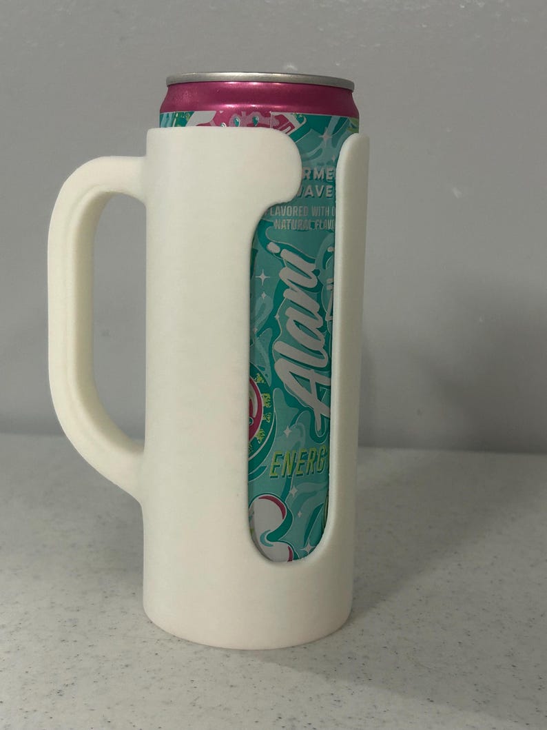 May include: A white 3D-printed can holder with a handle, designed to fit a standard beverage can. The can is visible through the holder's cutout, featuring a teal and pink label with the word "Alani".