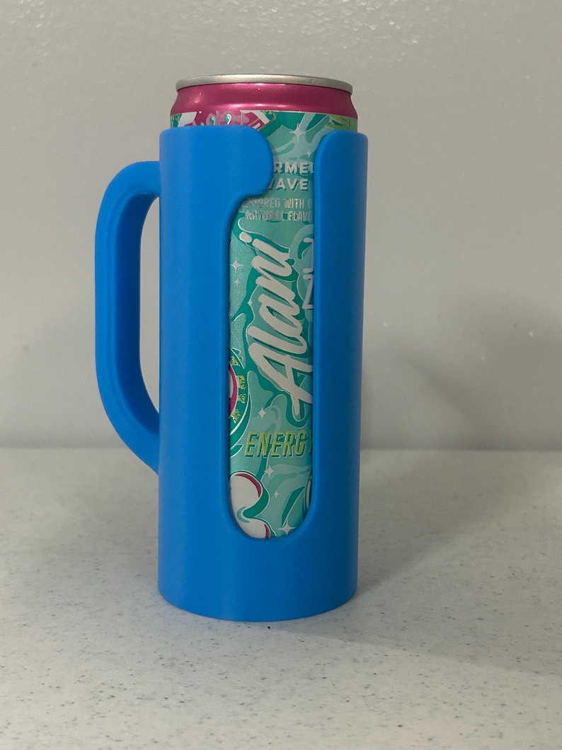 May include: A blue can cooler with a handle, holding a can of Alani Nu Energy drink. The can is pink and teal with the Alani Nu logo visible. The cooler is made of plastic and designed to keep beverages cold.