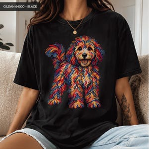 May include: A black short-sleeve t-shirt featuring a graphic of a multi-colored, vibrant dog with curly fur. The text GILDAN 64000 - BLACK is printed in the top left corner. The dog is depicted with red, blue, yellow, and orange brushstroke patterns.