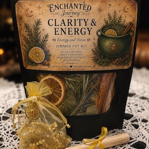 May include: A black pouch labeled Enchanted Journey Clarity & Energy Simmer Pot Kit with dried herbs, citrus slices, and cinnamon sticks. Includes a gold organza bag with gold metallic pieces and a small rolled parchment tied with a yellow ribbon.