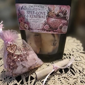May include: A black pouch labeled Enchanted Journey Self-Love & Renewal Simmer Pot Kit with a net weight of 2 oz, a small pink organza bag filled with pink crystals and a heart charm, and a rolled parchment paper tied with a light pink ribbon.