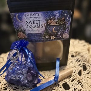 May include: A black pouch labeled Enchanted Journey Sweet Dreams Simmer Pot Kit with a blue organza bag containing purple stones and a silver moon charm, plus a cinnamon stick tied with a blue ribbon, all featuring celestial and botanical imagery.