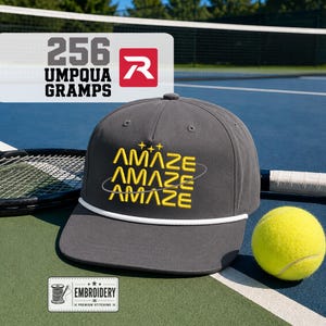 May include: A charcoal gray baseball cap with a white rope trim across the base of the crown. The front features the yellow embroidered text AMAZE repeated three times, stacked vertically, with small yellow star accents and a thin gray orbit line.