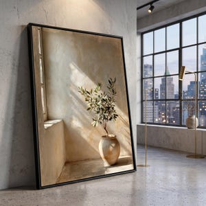 Op de afbeelding: Een groot rechthoekig ingelijst kunstwerk aan de muur met een afbeelding van een kleine olijfboom in een pot in een hoek, waarbij zonlicht schaduwen werpt op een getextureerde beige muur. De lijst is dun en zwart en omsluit het kunstwerk.