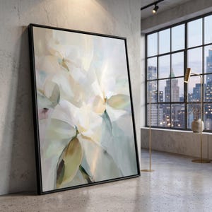Puede incluir: Una gran pieza de arte mural cuadrada que presenta una pintura floral abstracta con pinceladas suaves en tonos crema, blanco, verde pálido y oro apagado, encerrada en un marco negro fino, mostrada en una orientación vertical.
