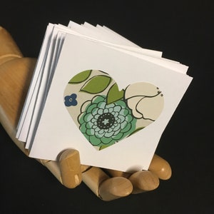 May include: A stack of white cards with a heart-shaped cutout. The cutout is filled with a green, blue, and white floral pattern.