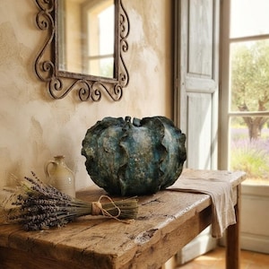 Può includere: Una scultura in ceramica rotonda e testurizzata con un bordo arricciato simile a un cavolo in tonalità blu profondo e verde. L'oggetto presenta una finitura maculata e usurata con creste visibili e un dettaglio centrale sulla sommità.