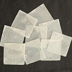 May include: A collection of translucent, square-shaped flat components made of a pale, cloudy material. Each square piece features one or two small, circular pre-drilled holes near the edges, designed for threading or connecting multiple pieces together.