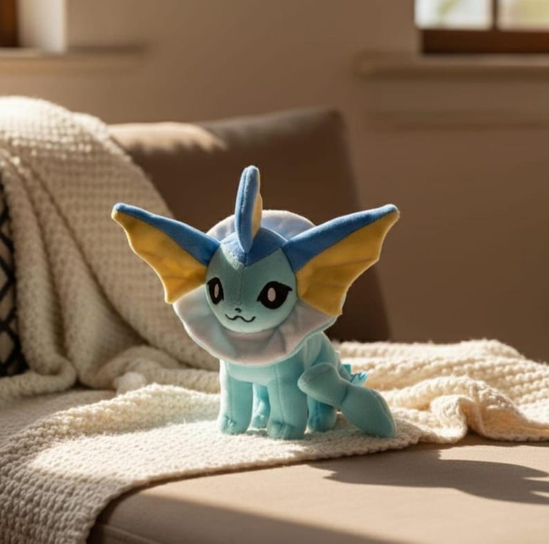 May include: A plush toy of a blue and yellow creature with large ears and a fin. The toy has a white collar and a small tail. It is sitting on a cream-colored blanket.