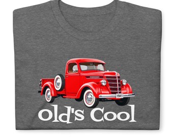 May include: A dark heather gray t-shirt featuring a graphic of a bright red 1941 vintage pickup truck with white-walled tires. Below the truck, the text "old's Cool" is printed in a bold, white, serif font across the chest of the garment.
