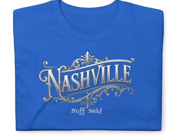 May include: A royal blue t-shirt featuring a metallic silver graphic design. The text reads "NASHVILLE" in a stylized, ornate font with decorative flourishes, and the words "Nuff Said" are printed in a smaller, simpler font directly below.