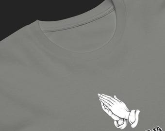 May include: A grey crew neck t-shirt featuring a white graphic of two hands pressed together in prayer. Below the graphic, the text "Matthew 5:14" is printed in a bold, white, sans-serif font. The design is positioned on the lower right side.
