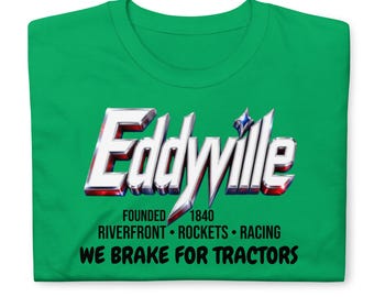 May include: A bright green t-shirt featuring the word Eddyville in a metallic, chrome-style font. Below the text, it reads FOUNDED 1840, RIVERFRONT ROCKETS RACING, and the phrase WE BRAKE FOR TRACTORS in bold black lettering across the chest area.