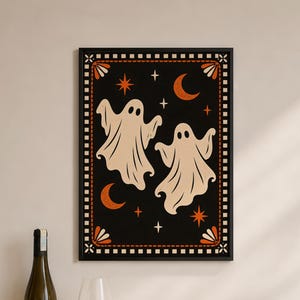 Peut inclure: Une impression d'art encadrée rectangulaire représentant deux fantômes beiges sur un fond noir, entourés de croissants de lune et d'étoiles orange. La bordure présente un motif à damier noir et blanc avec des accents en éventail orange.