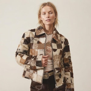 Könnte beinhalten: Eine Reißverschlussjacke aus einem Patchwork aus quadratischen Paneelen mit verschiedenen Brauntönen, Beige, Creme und weißen Felltexturen. Die Jacke hat einen klassischen Kragen, lange Ärmel und einen Metallreißverschluss in der vorderen Mitte.