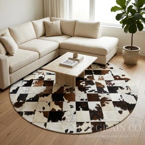 May include: A circular area rug constructed from square patches of cowhide in a checkerboard pattern of white, brown, and black. The rug features a visible watermark in the bottom right corner that reads FINE GRAIN CO. Hand Crafted Leather Goods.
