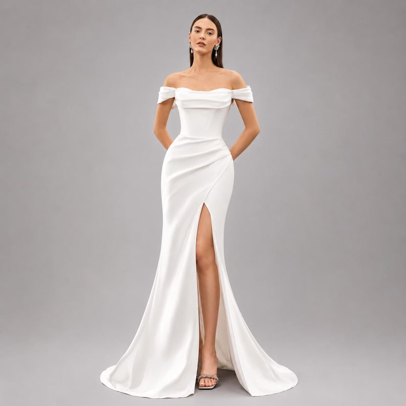 May include: A white off-the-shoulder wedding dress with a fitted bodice and a high slit. The dress has a flowing skirt that extends into a train. The model is wearing silver heels.