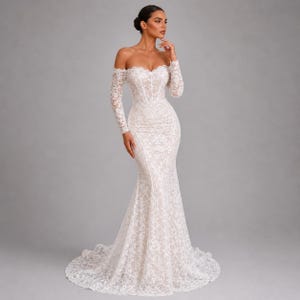 May include: A white lace wedding dress with an off-the-shoulder design and long sleeves. The gown has a fitted bodice and a mermaid skirt that flares out from the knees. The dress features a sweetheart neckline and a train.