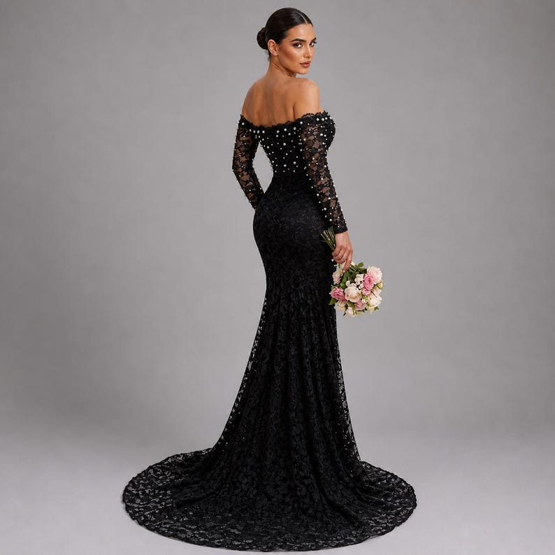 May include: A black lace, off-the-shoulder gown with long sleeves and a mermaid cut. The dress is adorned with pearls on the neckline and sleeves. The person is holding a bouquet of pink and white flowers. The dress has a long train.