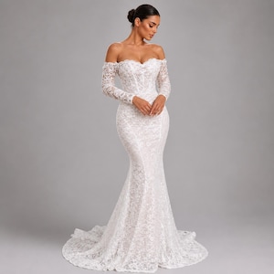 May include: A white, off-the-shoulder wedding dress with long sleeves. The dress is made of lace and has a mermaid silhouette, fitted through the bodice and flaring out from the knees. The dress features a sweetheart neckline and a train.
