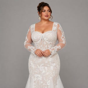 May include: A floor-length white gown featuring a sweetheart neckline, long sheer sleeves, and a corset-style bodice. The dress is adorned with intricate white floral embroidery and lace appliqu&eacute;s that extend from the bodice down to the skirt.