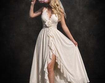 May include: A cream-colored halter dress featuring a ruffled neckline, a large fabric flower at the waist, and a high-low skirt with cascading ruffles along the front slit. The dress is made of a lightweight, flowing fabric with a sheer overlay.