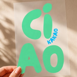 Könnte beinhalten: Ein rechteckiges, transparentes Blatt mit dem Wort CIAO in großen, abgerundeten, mintgrünen Buchstaben. Das Wort KAKAO ist in kleineren, hellblauen, serifenlosen Buchstaben vertikal zwischen den Buchstaben C und O aufgedruckt.