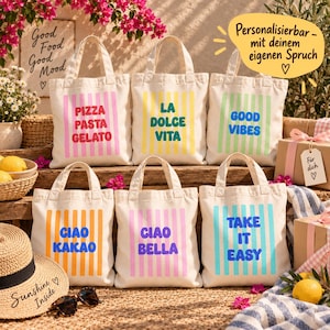 Könnte beinhalten: Sechs cremefarbene Canvas-Tragetaschen mit zwei Henkeln und vertikalen Streifen in Pink, Gelb, Grün, Orange und Blau. Die Taschen zeigen Texte in fetten, bunten Buchstaben: PIZZA PASTA GELATO, LA DOLCE VITA, GOOD VIBES, CIAO KAKAO, CIAO BELLA und TAKE IT EASY.