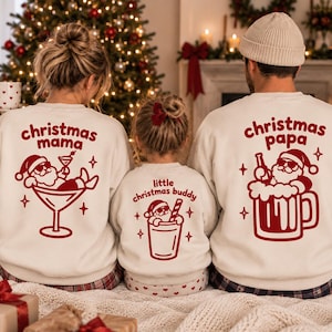 Puede incluir: Tres sudaderas de cuello redondo color blanco roto con estampados gráficos rojos. La sudadera de la izquierda dice christmas mama con un Santa en una copa de martini. La del centro dice little christmas buddy con un Santa en un vaso. La de la derecha dice christmas papa con un Santa en una jarra de cerveza.
