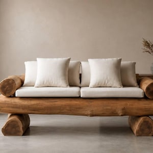 Könnte beinhalten: Rustikales Holzsofa mit einem Sockel und Armlehnen aus Naturstämmen. Das Sofa hat ein helles Kissen und vier quadratische, cremefarbene Kissen. Das Design ist minimalistisch und das Sofa steht in einem Raum mit neutralen Farbtönen. Ca. 200 cm lang.