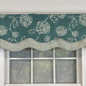 May include: A teal valance with a white floral pattern and a scalloped bottom edge. The valance has a white and gray striped trim.