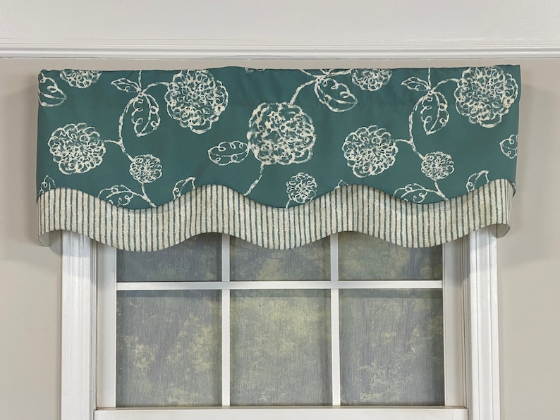 May include: A teal valance with a white floral pattern and a scalloped bottom edge. The valance has a white and gray striped trim.