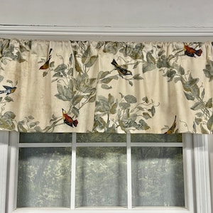 May include: A cream-colored valance with a leafy pattern and colorful birds. The valance is hung on a window with white trim.