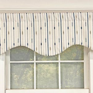 May include: A valance with a cream background and vertical stripes in blue and tan. The valance is above a white window with a grid pattern. The bottom edge of the valance has a scalloped design.