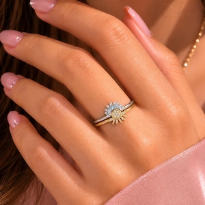 Könnte beinhalten: Ein zweiteiliges Ring-Set bestehend aus einem silberfarbenen Ring mit einem halbkreisförmigen Sonnenstrahlen-Design, das mit kleinen klaren Steinen besetzt ist, und einem goldfarbenen Ring mit einem passenden Sonnenmotiv und klaren Steinen.