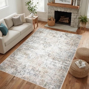May include: A large rectangular area rug with a distressed, abstract design in shades of white, gray, and brown. The rug is placed on a hardwood floor, and the room features a sofa, fireplace, and decorative poufs.