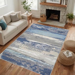 Peut inclure: Un tapis rectangulaire présentant un motif abstrait et usé avec des bandes horizontales bleu marine, bleu clair, gris ardoise et crème. Le design imite une texture vieillie avec des intensités de couleur variées sur toute la surface.