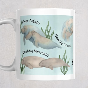 May include: A white ceramic mug featuring a light blue background with illustrations of manatees and green seaweed. The text reads River Potato, Gentle Giant, and Chubby Mermaid. The design includes multiple manatees in various swimming positions.