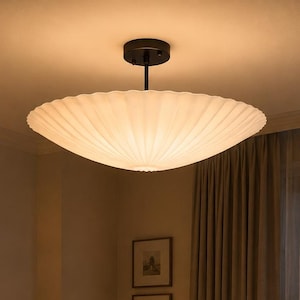 May include: A semi-flush mount ceiling light fixture featuring a large, circular, pleated white shade with a soft, diffused glow. The shade is suspended from the ceiling by a thin, black metal rod and a matching circular black canopy mount.