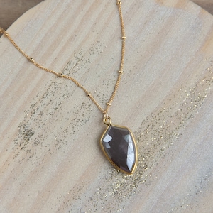 May include: A gold chain necklace with a large, faceted, dark gray gemstone pendant. The pendant is shaped like a teardrop.