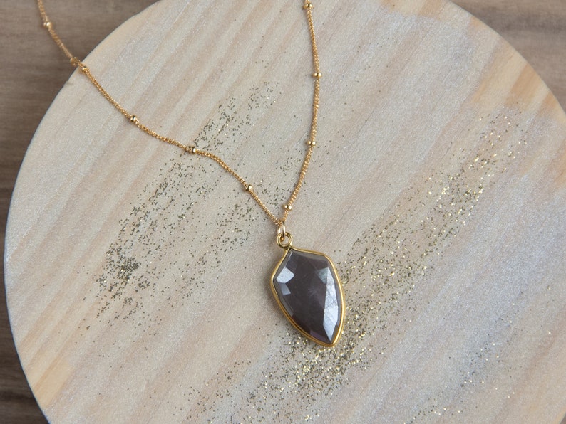 May include: A gold chain necklace with a large, faceted, dark gray gemstone pendant. The pendant is shaped like a teardrop.